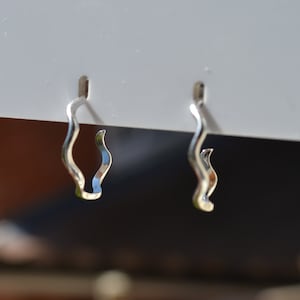 May include: A pair of silver hoop earrings with a wavy design. The earrings are hanging from a white display card.