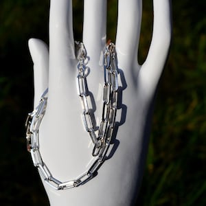 May include: A silver chain necklace with a box chain design. The chain is made of interlocking rectangular links.