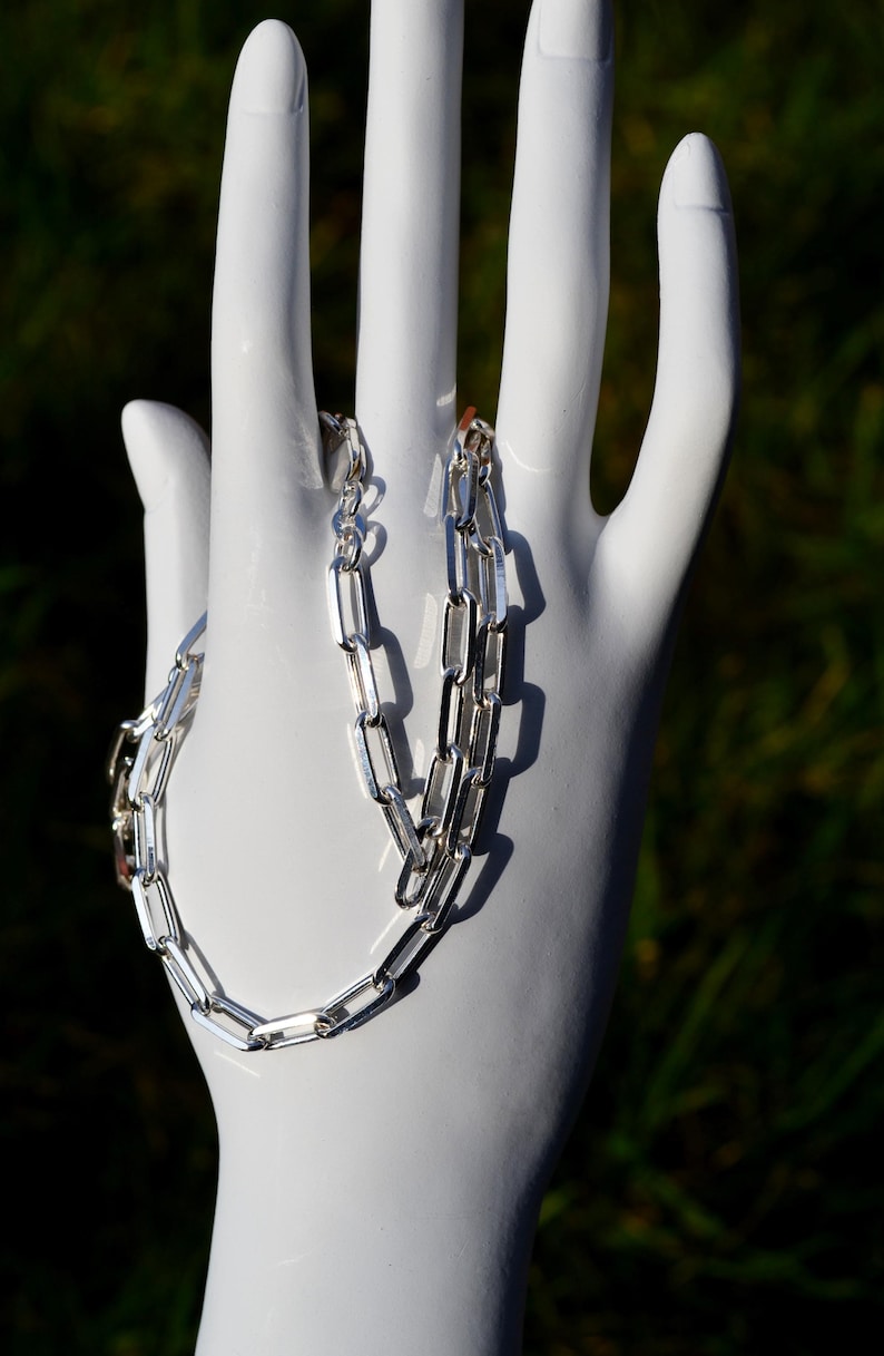 May include: A silver chain necklace with a box chain design. The chain is made of interlocking rectangular links.