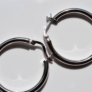 May include: A pair of silver hoop earrings with a hinged clasp. The earrings are simple and elegant.