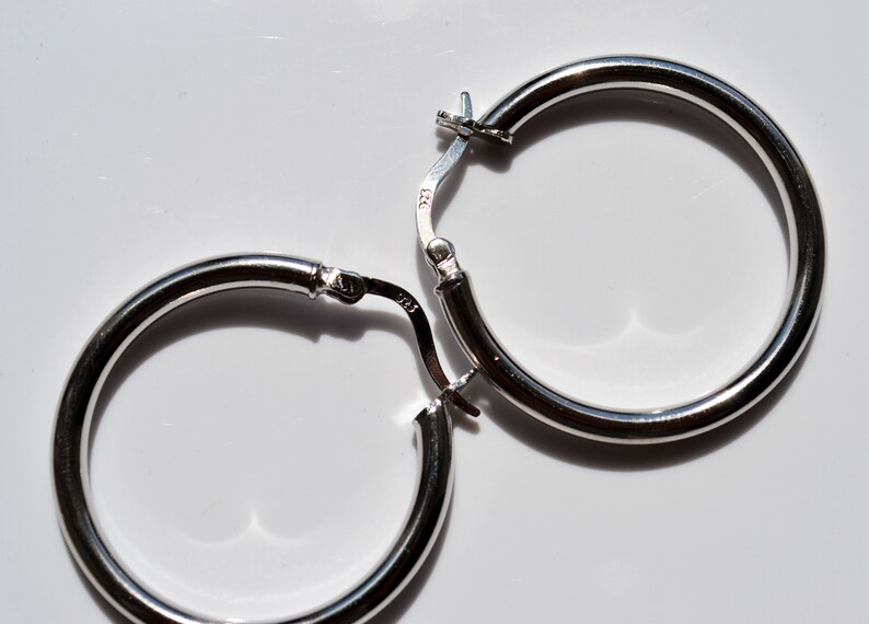 May include: A pair of silver hoop earrings with a hinged clasp. The earrings are simple and elegant.
