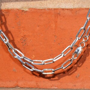 May include: A silver chain necklace with a lobster clasp fastening. The chain is made of interlocking oval links.