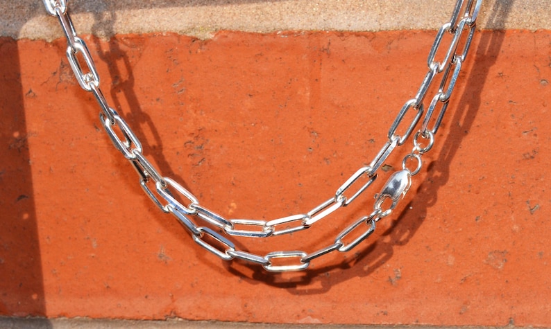 May include: A silver chain necklace with a lobster clasp fastening. The chain is made of interlocking oval links.
