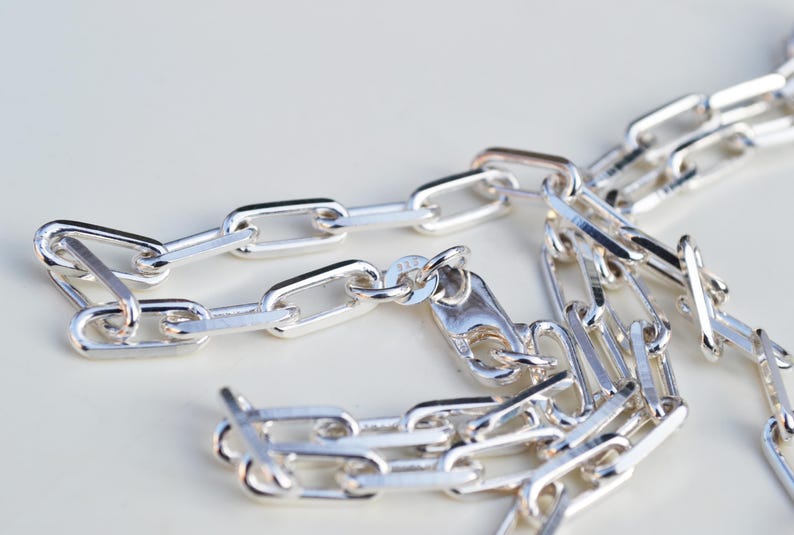 May include: A silver chain necklace with a lobster clasp fastening. The chain is made of interlocking oval links.