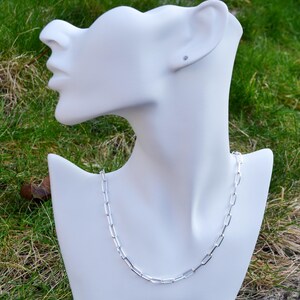 May include: A silver chain necklace with a box chain design. The chain is on a white mannequin bust.
