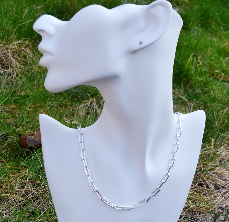 May include: A silver chain necklace with a box chain design. The chain is on a white mannequin bust.