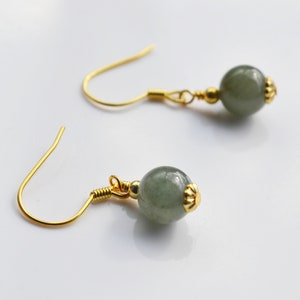K&ouml;nnte beinhalten: Ein Paar goldene Ohrringe mit gr&uuml;nen Edelsteinperlen. Die Ohrringe haben ein schlichtes Design mit einer kleinen goldenen Perle an der Oberseite des Edelsteins.