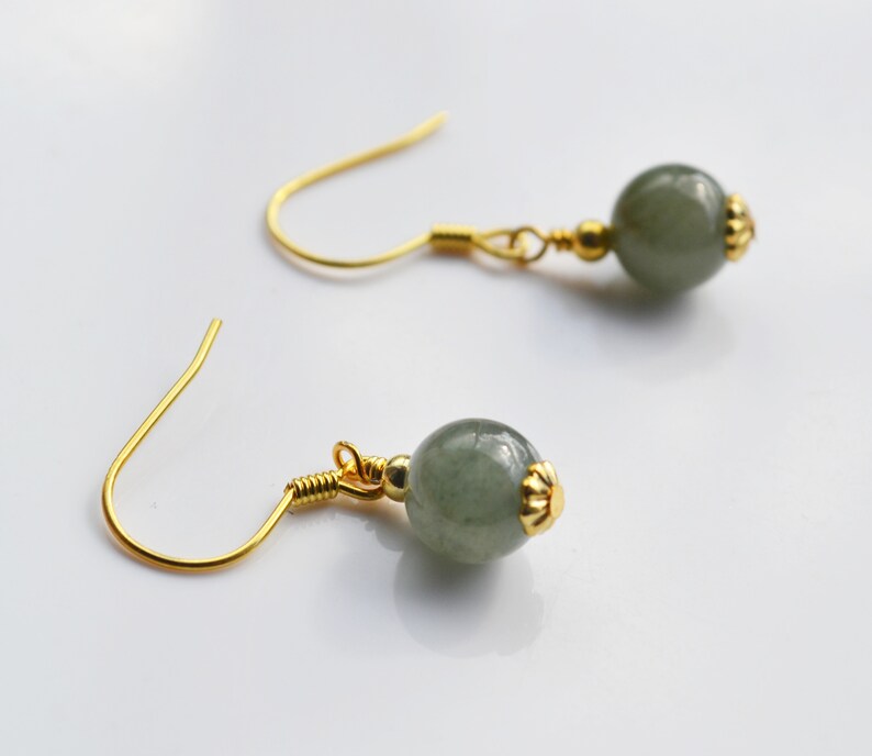 K&ouml;nnte beinhalten: Ein Paar goldene Ohrringe mit gr&uuml;nen Edelsteinperlen. Die Ohrringe haben ein schlichtes Design mit einer kleinen goldenen Perle an der Oberseite des Edelsteins.