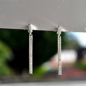 May include: A pair of silver dangle earrings with a long, thin bar design. Each bar is lined with small, clear cubic zirconia stones.