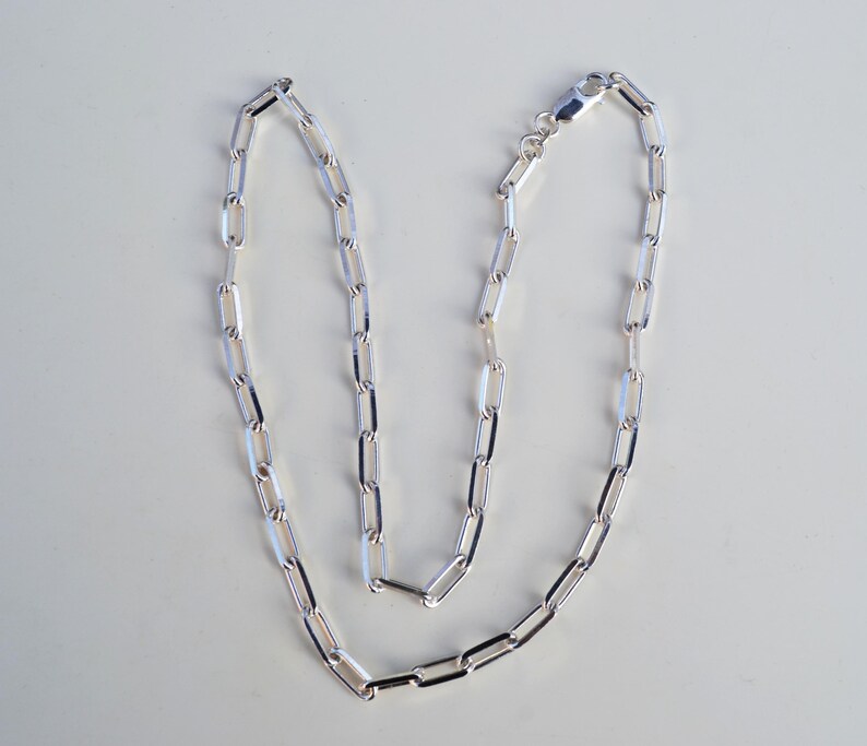 May include: A silver chain necklace with a simple, linked design. The chain is made of small, rectangular links.
