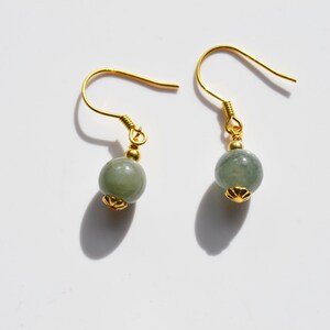 K&ouml;nnte beinhalten: Ein Paar goldene Ohrringe mit gr&uuml;nen Jade-Perlen. Die Ohrringe haben ein schlichtes Design mit einer kleinen goldenen Perle an der Oberseite des Jade-Steins.