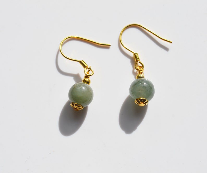 K&ouml;nnte beinhalten: Ein Paar goldene Ohrringe mit gr&uuml;nen Jade-Perlen. Die Ohrringe haben ein schlichtes Design mit einer kleinen goldenen Perle an der Oberseite des Jade-Steins.