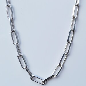 May include: A silver chain necklace with a link style that resembles a paperclip. The chain is made of polished metal and has a smooth, shiny finish.