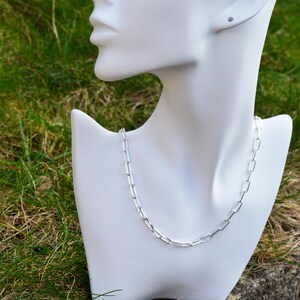 May include: A silver chain necklace with a simple, rectangular link design. The necklace is displayed on a white mannequin bust.