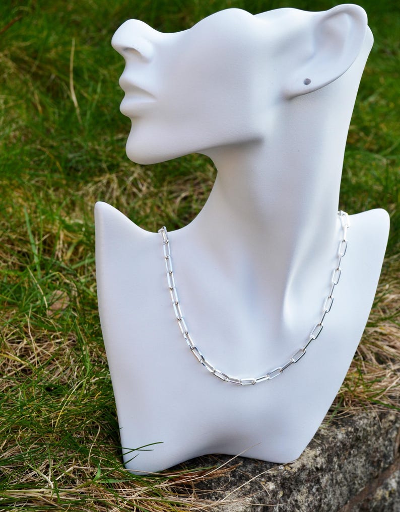 May include: A silver chain necklace with a simple, rectangular link design. The necklace is displayed on a white mannequin bust.