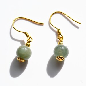 K&ouml;nnte beinhalten: Ein Paar goldene Ohrringe mit gr&uuml;nen Jade-Perlen. Die Ohrringe haben ein schlichtes Design mit einer kleinen goldenen Blumenverzierung an der Unterseite jeder Perle.