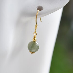 K&ouml;nnte beinhalten: Ein goldener Ohrh&auml;nger mit einer einzigen runden gr&uuml;nen Edelsteinperle.