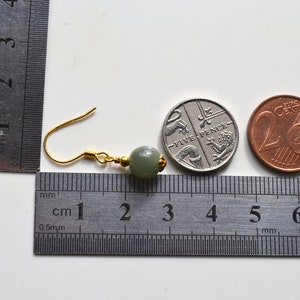 K&ouml;nnte beinhalten: Ein Paar gr&uuml;ne Jade-Ohrringe mit goldenen Haken. Die Ohrringe werden neben einem Lineal und zwei M&uuml;nzen gezeigt, einer britischen F&uuml;nf-Pence-M&uuml;nze und einer 20-Cent-Euro-M&uuml;nze, als Gr&ouml;&szlig;envergleich.