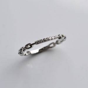 May include: A silver ring with a chain design and a row of small clear stones.