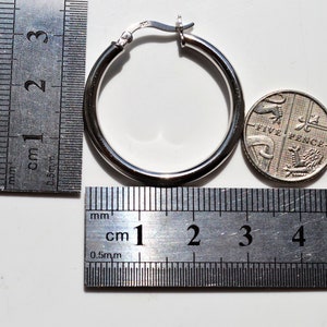 May include: Silver hoop earrings with a diameter of approximately 2.5 cm, shown next to a ruler and a British five pence coin.