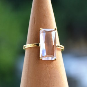 May include: A gold ring with a large, clear, rectangular gemstone.