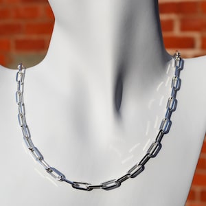 May include: A silver chain necklace with a link style that resembles paper clips. The chain is on a white mannequin.