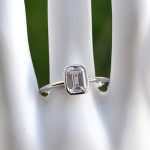 May include: A silver ring with a clear emerald-cut gemstone.