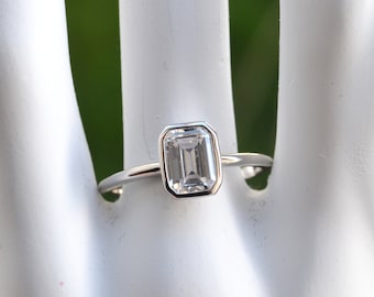 May include: A silver ring with a clear emerald-cut gemstone.