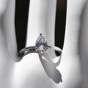 May include: A silver ring with a pear-shaped clear gemstone.