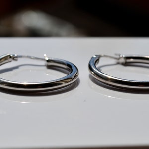 May include: A pair of silver hoop earrings. The earrings are smooth and have a simple design.