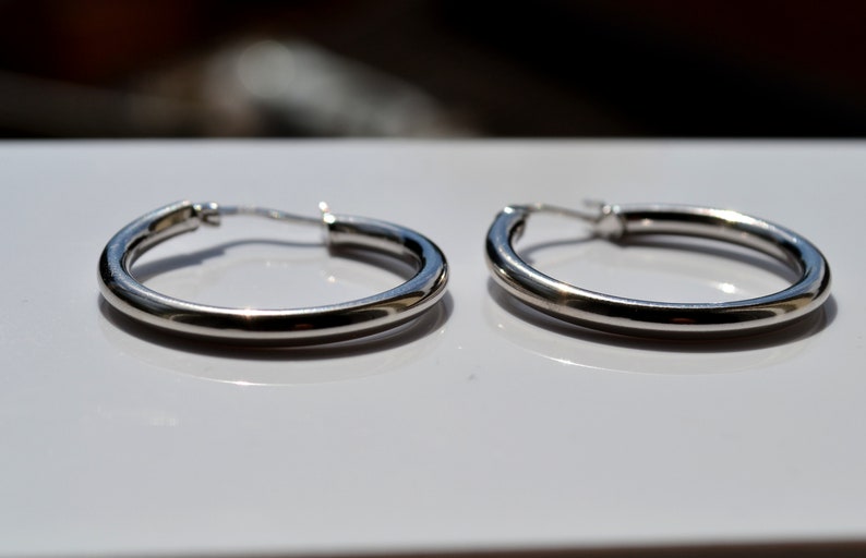 May include: A pair of silver hoop earrings. The earrings are smooth and have a simple design.