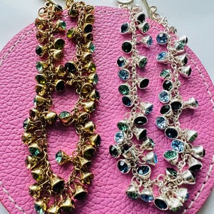 May include: Two multi-strand bracelets with dangling charms. One bracelet is gold with green and black crystals. The other bracelet is silver with blue and black crystals.