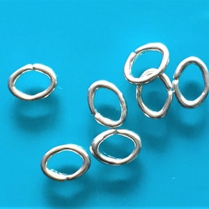 Pode incluir: Argolas de salto de prata, de forma oval, sobre um fundo azul.