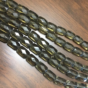 May include: A strand of faceted smoky quartz beads. The beads are rectangular in shape and have a dark grey colour.