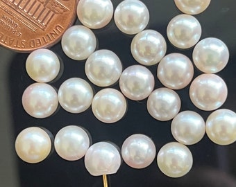 May include: A collection of 18 white round pearls, some with iridescent shimmer, scattered on a black surface. A US penny coin is included for size reference.