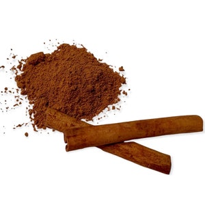 May include: A pile of ground cinnamon with two cinnamon sticks on a white background.