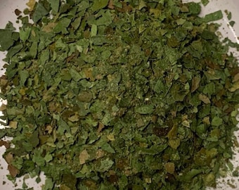 May include: A white ceramic plate with a green pile of dried herbs in the center.