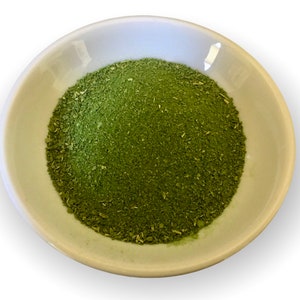 May include: A small white bowl filled with a generous amount of finely ground green powder.