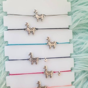 May include: Six colourful string bracelets with silver llama charms. The bracelets are displayed on a white background.