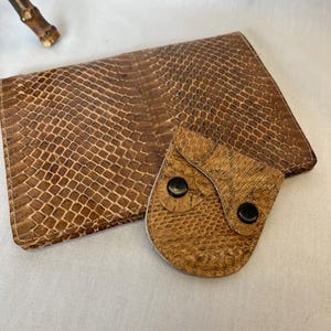 May include: A brown leather wallet with a snakeskin pattern and a small flap pocket with two black buttons.
