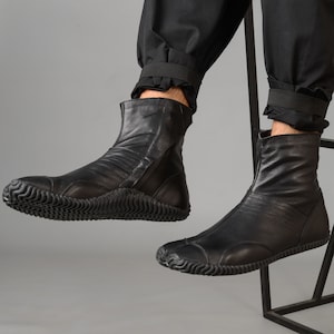May include: Black leather ankle boots with a zipper on the side and a thick rubber sole. The boots have a pointed toe and a slightly raised heel.