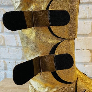 May include: Gold leather boots with black velcro straps and silver buckles.