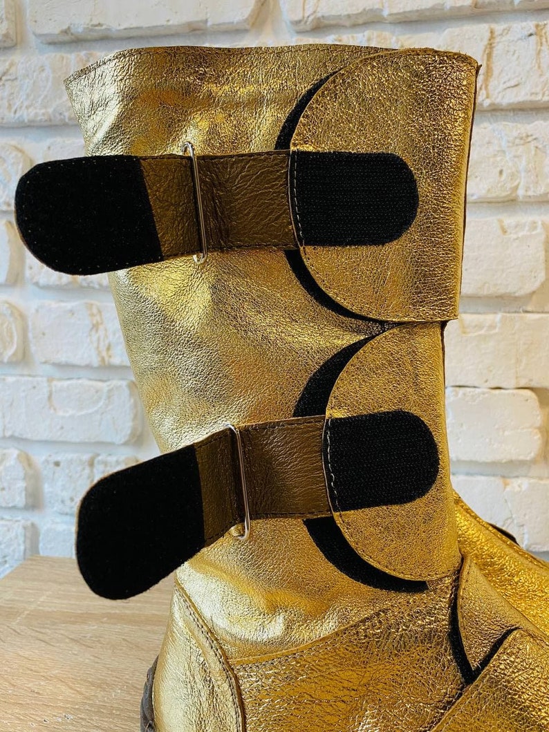 May include: Gold leather boots with black velcro straps and silver buckles.