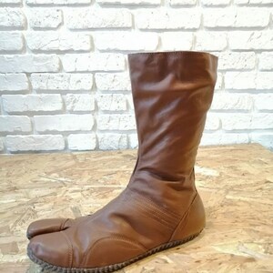 Puede incluir: Botas de cuero marr&oacute;n con un dise&ntilde;o de punta dividida. Las botas tienen un eje alto y una punta redonda.
