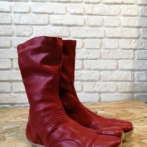 Pu&ograve; includere: Un paio di stivali in pelle rossa con un design a punta divisa. Gli stivali hanno una cerniera sul retro e una suola in gomma spessa.