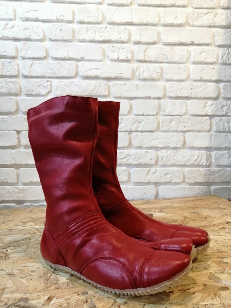 Pu&ograve; includere: Un paio di stivali in pelle rossa con un design a punta divisa. Gli stivali hanno una cerniera sul retro e una suola in gomma spessa.