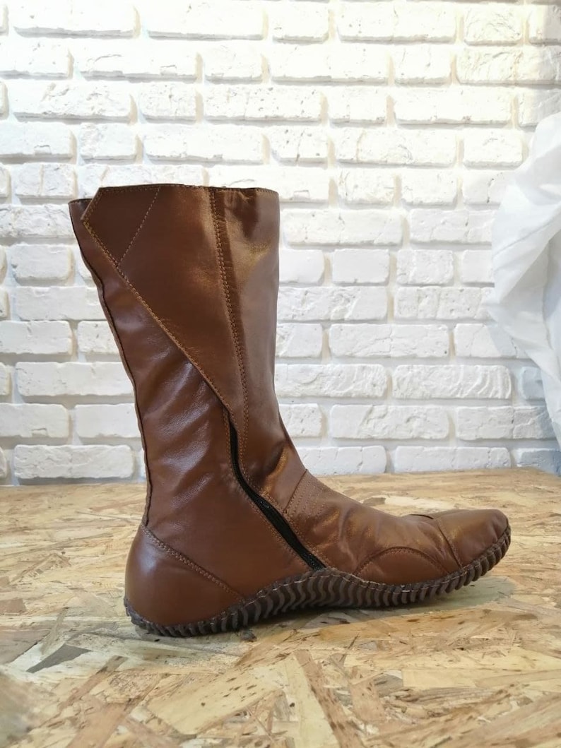 Puede incluir: Botas de cuero marr&oacute;n de ca&ntilde;a alta con cremallera lateral y suela texturizada.