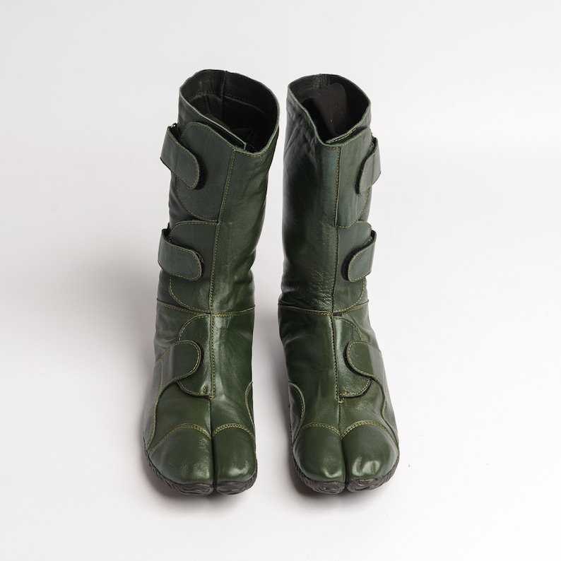 Puede incluir: Un par de botas de cuero verde oscuro con m&uacute;ltiples correas y un dise&ntilde;o de punta dividida.