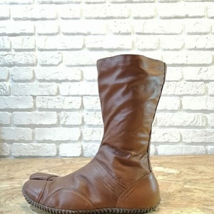 Puede incluir: Botas de cuero marr&oacute;n con un dise&ntilde;o de punta dividida. Las botas son de altura por encima de la rodilla y tienen un estilo simple y elegante.