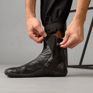 May include: Black leather ankle boots with a zipper and a textured sole. The boots are being pulled on by a person.